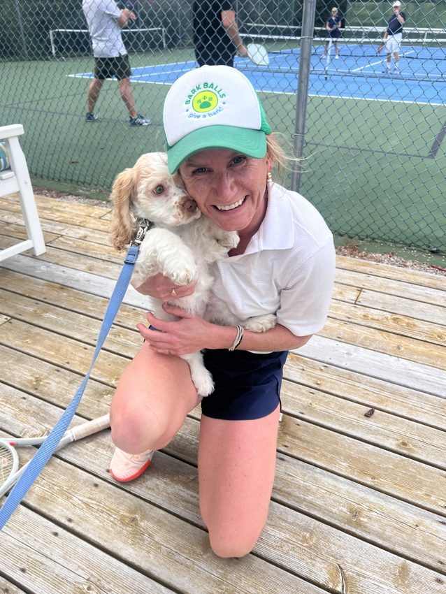 A Bark Baller hugging a puppy courtside at a tennis club