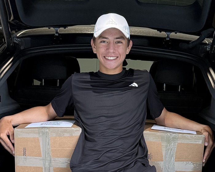 Alejandro Palacios with two boxes of collected tennis balls packed for shipment